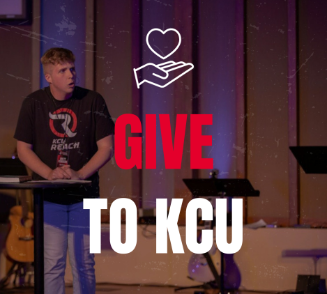 A person standing at a podium with "GIVE TO KCU" text and heart and hand icons overlaid on the image.