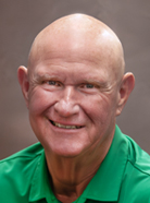 Bald man wearing a green polo shirt, smiling in front of a neutral background.